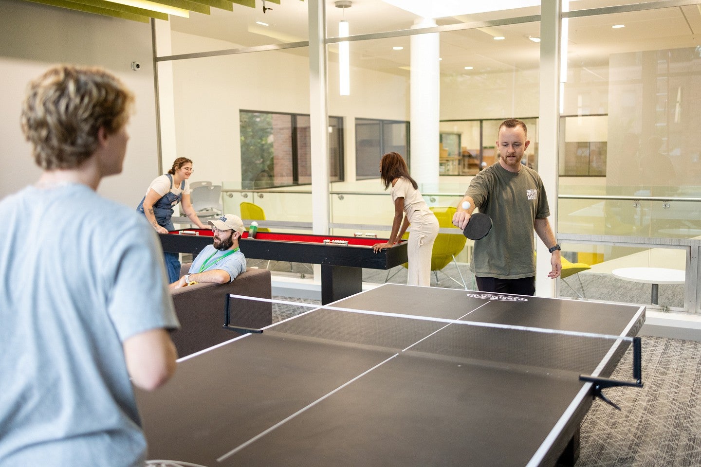 students play ping pong, shuffleboard, and sit on a couch in the Duck Den