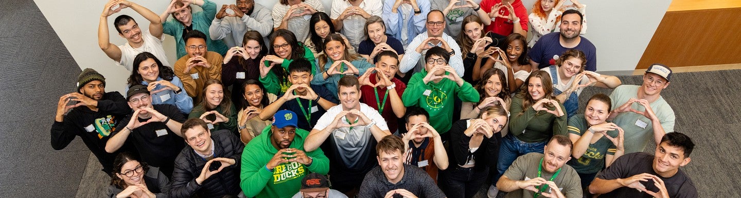 Students pose in the lobby of the campus center, holding up their hands in an O-shape and smiling