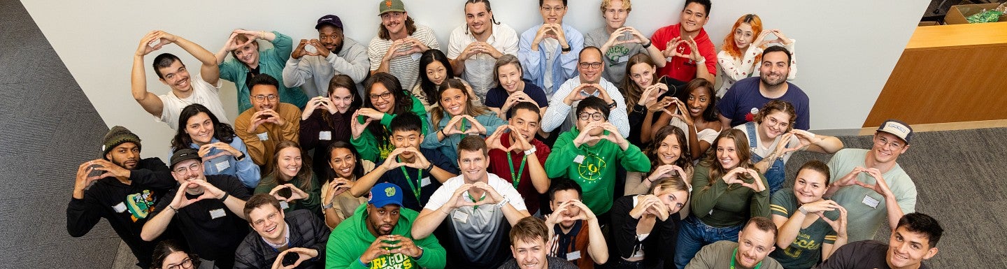 Students pose in the lobby of the campus center, holding up their hands in an O-shape and smiling