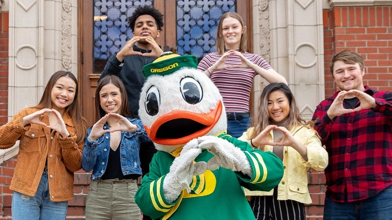 Students and the UO Duck make the O symbol with their hands