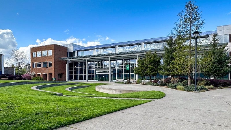 Outside of the Library and Learning Center on the UO Portland campus. A pathway splits to a Y, with the left path going to a small amphitheater in the grass and the right path going out of the photo. 