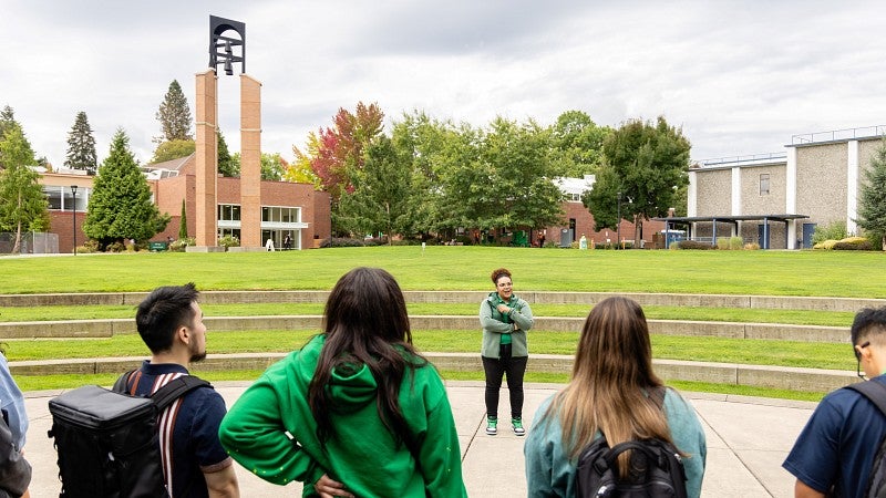 A tour guide speaks to a group of students in the amphitheatre of the campus green. The bell tower is visible in the background.