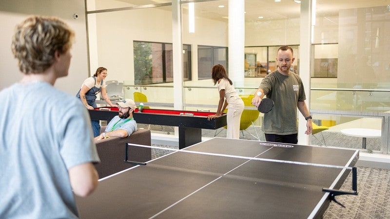 students play ping pong, shuffleboard, and sit on a couch in the Duck Den