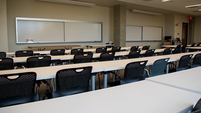 The front of the classroom has multiple large white boards and two projector screens. 