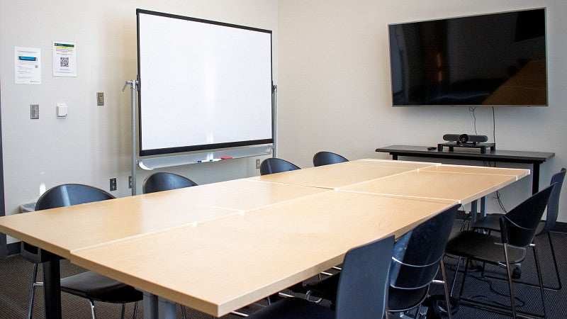 Eight chairs around the conference table, as well as a movable white board and display screen. 