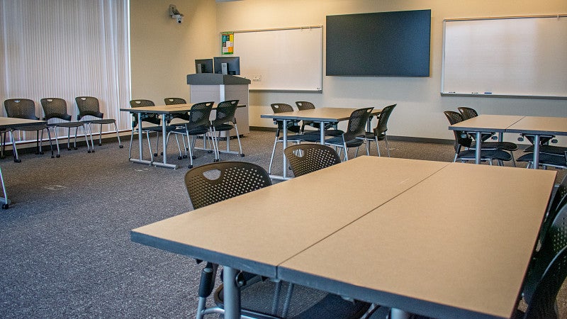 The classroom has multiple white boards and two large windows. 