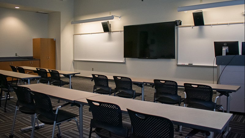 The classroom includes multiple screens and white boards. 
