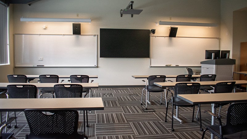 The classroom includes multiple screens and white boards. 
