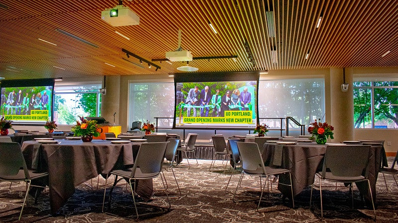 The event space set with round tables, a stage and multiple projection screens. 