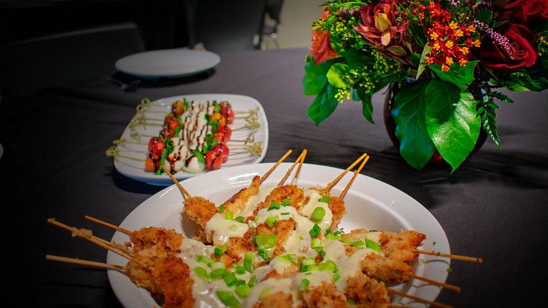Table set for a reception with appetizers and flowers on a black tablecloth