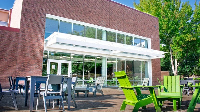Patio of Campus Center has grey tables and green lounge chairs.