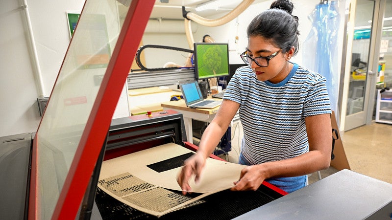 A student moves a sheet of wood in the CNC machine in the Fabrication Lab.
