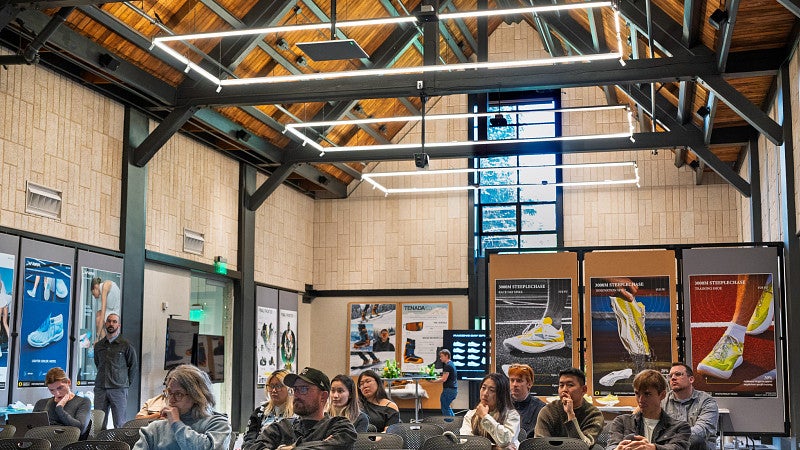 Students in the Innovation Commons during a final review for Sports Product Design. The room has displays of student work and the room has a tall, vaulted ceiling.