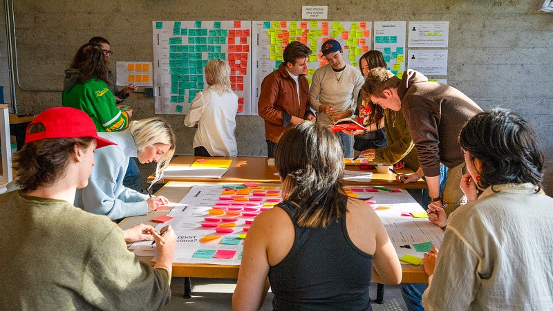 Product design students sit around a table making notes on bright colored paper. 