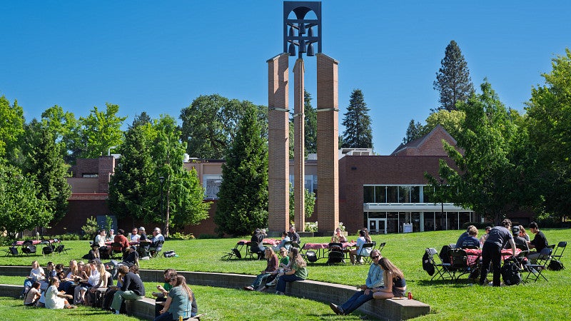 People sit at the outdoor amphitheater during an event on the campus green. The bell tower is in the background. 