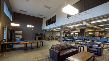 Before photo of the UO Portland Campus Center shows the exterior entry into the dining room. Couches are in the forefront with tables in the background. A second level cuts into the space with windows looking over the area. 