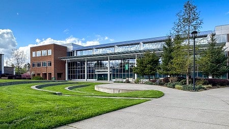 Outside of the Library and Learning Center on the UO Portland campus. A pathway splits to a Y, with the left path going to a small amphitheater in the grass and the right path going out of the photo. 