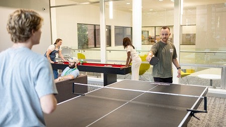 students play ping pong, shuffleboard, and sit on a couch in the Duck Den