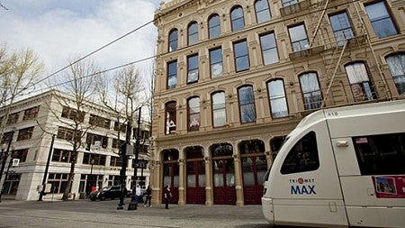 A Trimet Max train runs in front of the White Stag building.