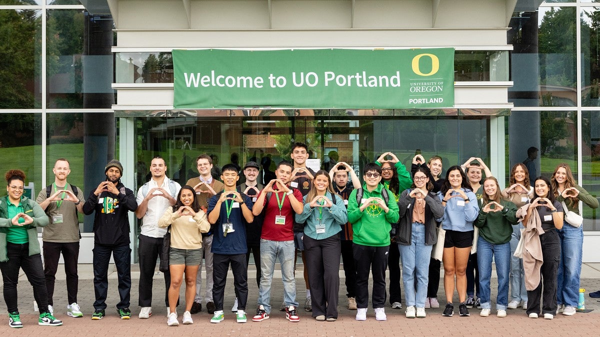 Students pose in front of the library, holding their hands in an O shape and smiling