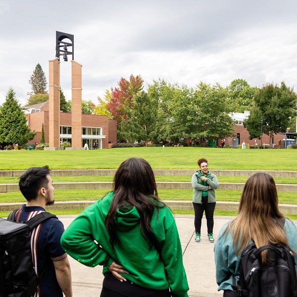 A tour guide speaks to a group of students in the amphitheatre of the campus green. The bell tower is visible in the background.