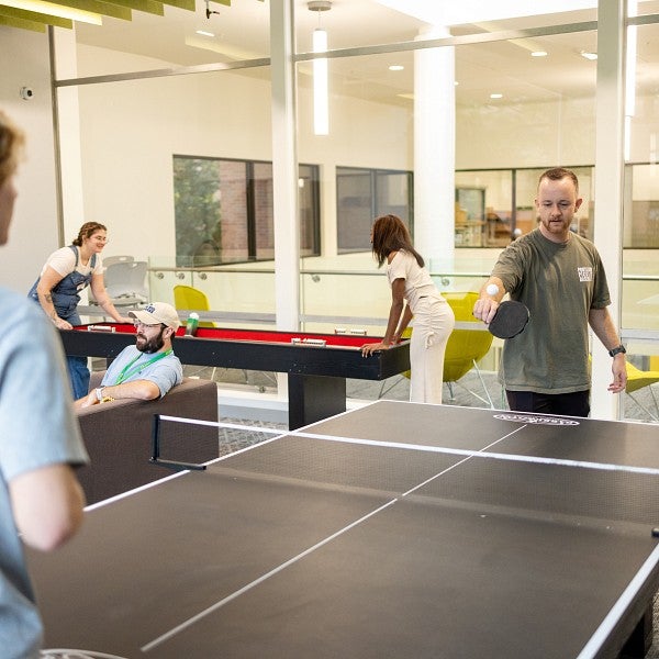 students play ping pong, shuffleboard, and sit on a couch in the Duck Den