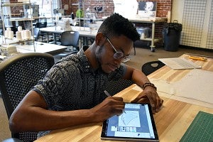 A sports product design student sketches a shoe on a tablet 