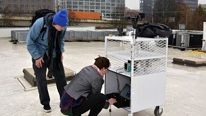 Elise Braun, right, and Thomas Cooper collect data from a weather station on the roof of Opsis Architecture, as a semitruck drives by on Interstate 405. Collecting rooftop data