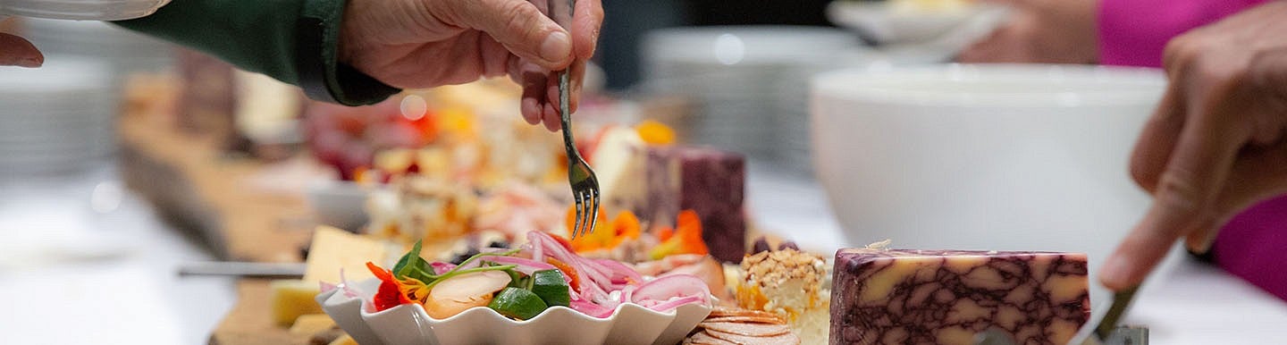 Attendees take vegetables and cheese from a buffet table. 